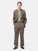 Model standing in studio wearing the AURALEE Light Wool Max Gabardine Two-Tuck Slacks Dark in Olive Brown