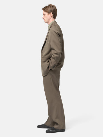 side view of the Model standing in studio wearing the AURALEE Light Wool Max Gabardine Two-Tuck Slacks Dark in Olive Brown