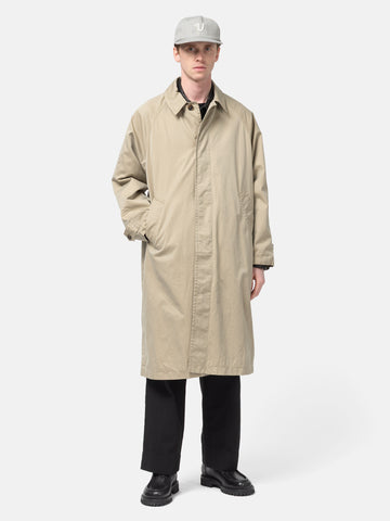 Model standing in studio wearing the UNLIKELY Balmacaan Coat in Beige