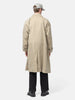 Rear view of the Model standing in studio wearing the UNLIKELY Balmacaan Coat in Beige