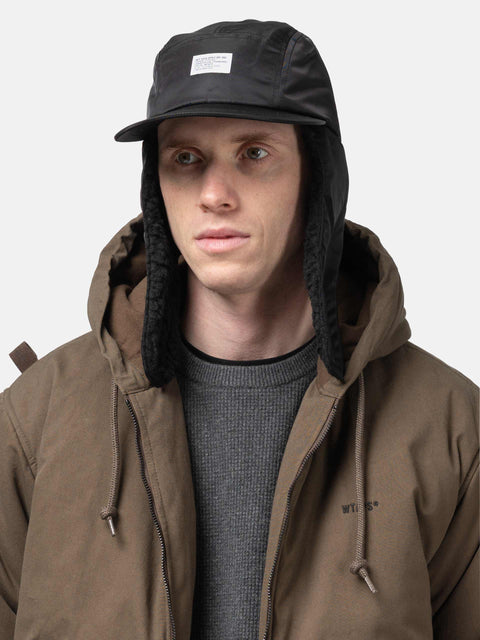 Model is wearing WTAPS AVT Cap  Nylon Satin Cordura in Black with ear flap down